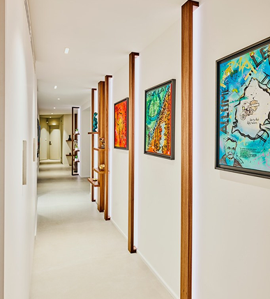 Long couloir aménagé et décoré de tableaux ponctués de tasseaux en noyer éclairés