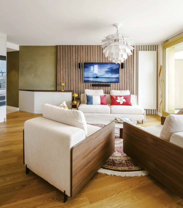 Salon lumineux avec canapés et meuble sur-mesure entouré de panneaux en noyer sur lesquels repose la TV